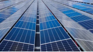 Vista aérea de um galpão industrial moderno com o telhado totalmente coberto por fileiras de placas solares fotovoltaicas brilhando sob a luz do sol.